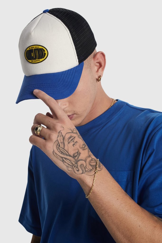 Homem com boné e camiseta azul, mostrando tatuagens.
