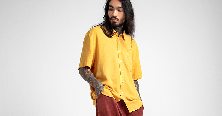 Homem com camisa amarela posando em fundo neutro
