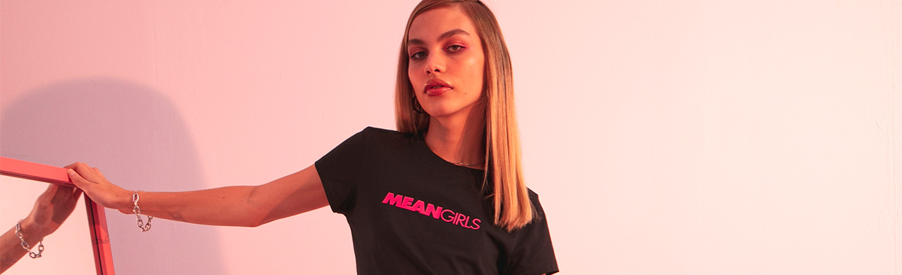 Modelo feminina com camiseta MEAN GIRLS em fundo rosa