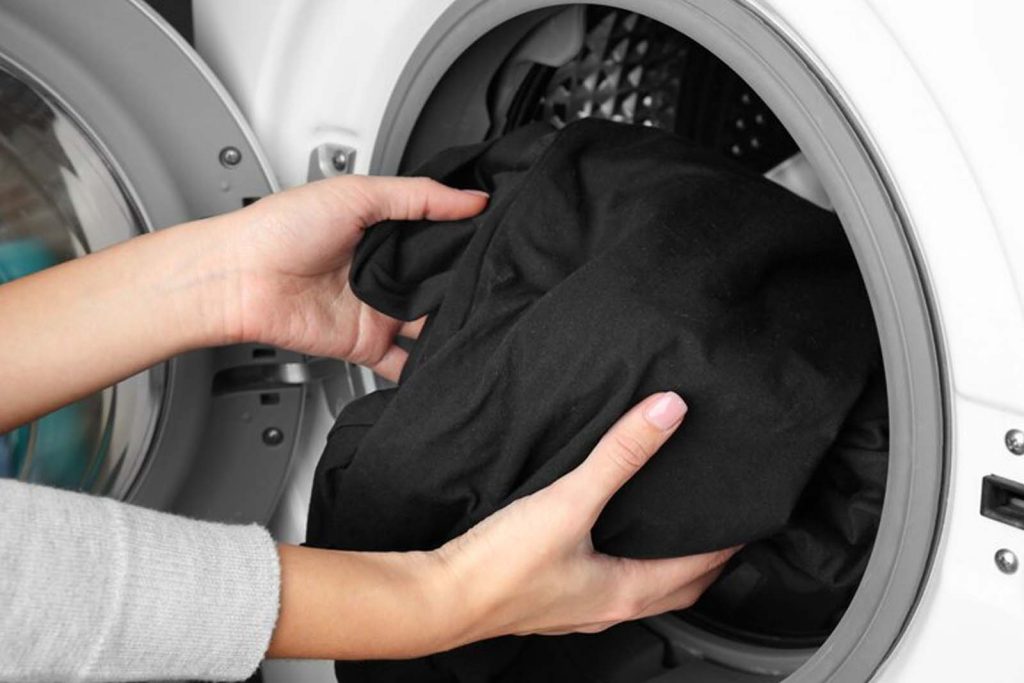 Imagem de uma modelo inserindo roupas pretas na maquina de lavar