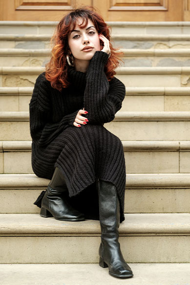 Mulher com cabelo encaracolado usando vestido preto sentada em escada